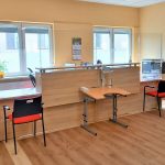 Pomieszczenie Centrum Wsparcia, miejsce przyjmowania dokumentów oraz obsługi studentów. Na zdjęciu trzy stanowiska do obsługi studentów, jedno wyposażone w lupę elektroniczną udźwiękowioną oraz stolik dla osób poruszających się na wózku inwalidzkim.