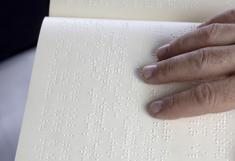 Po kartce z wydrukowanym tekstem w alfabecie Braille'a palcami przesuwa się męska dłoń.