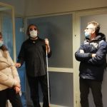 Przewodnik ubrany w ciemne okulary opowiada o dostosowaniu materiałów. Wokół niego stoją słuchacze.