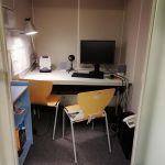 Boks, w którym jest biurko z komputerem, mikrofonem, lampką, szafką i telefonem.