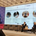 Prelegentki omawiają prezentację o realizacji projektu. W tle duży slajd ze sprzętem specjalistycznym, znajdującym się w pracowni wsparcia. Dwoje moderatorów przysłuchuje się wystąpieniu, jedna osoba tłumaczy na Polski Język Migowy.