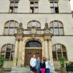 Uśmiechnięci pracownicy UJK pozują do zdjęcia, w tle budynek Rektoratu Collegium Minus Uniwersytetu Adama Mickiewicza w Poznaniu.