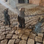 Figury wrocławskich krasnali symbolizujące trzy rodzaje niepełnosprawności: słuchu, wzroku i ruchu. Wokół jest zabudowa miasta.