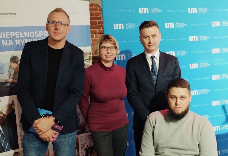 Troje pracowników Centrum Wsparcia i współorganizator Konferencji pozują do zdjęcia w sali konferencyjnej. Za nimi stoją roll-upy.