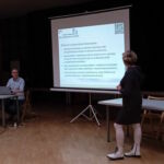 Kierownik Centrum Wsparcia omawia wyświetlaną na rzutniku ofertę wsparcia dla pracowników UJK. Obok przy stoliku siedzi mgr Sebastian Grabek obsługujący wyświetlaną prezentację.