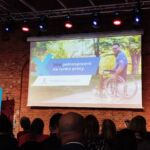 Sala konferencyjna. Uczestnicy spotkania słuchają wystąpienia zaproszonego gościa. Na ścianie na rzutniku powitalny napis "10 Konferencja (Nie)pełnosprawni na rynku pracy".