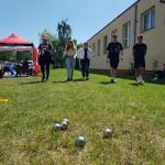 Rozgrywki w bule. Na pierwszym planie 5 metalowych kul - bul leży na trawie. Za nimi uczestnicy rozgrywek - 5 osób, idą w kierunku bul.